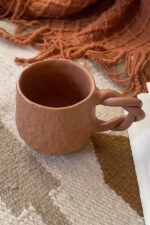Doro Stoneware Mug Where craft becomes texture you can feel A light brown stoneware mug with a hammered texture inspired by traditional copper work, and a hand-braided handle that adds a unique artisanal character.