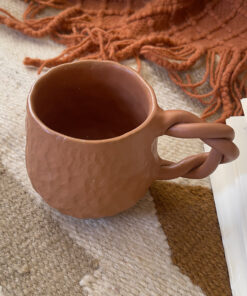 Doro Stoneware Mug Where craft becomes texture you can feel A light brown stoneware mug with a hammered texture inspired by traditional copper work, and a hand-braided handle that adds a unique artisanal character.