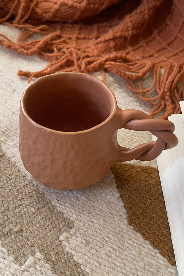 Doro Stoneware Mug Where craft becomes texture you can feel A light brown stoneware mug with a hammered texture inspired by traditional copper work, and a hand-braided handle that adds a unique artisanal character.