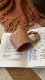 Doro Stoneware Mug Where craft becomes texture you can feel A light brown stoneware mug with a hammered texture inspired by traditional copper work, and a hand-braided handle that adds a unique artisanal character.