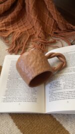 Doro Stoneware Mug Where craft becomes texture you can feel A light brown stoneware mug with a hammered texture inspired by traditional copper work, and a hand-braided handle that adds a unique artisanal character.