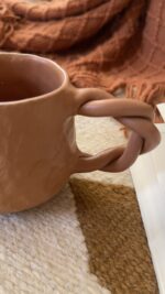 Doro Stoneware Mug Where craft becomes texture you can feel A light brown stoneware mug with a hammered texture inspired by traditional copper work, and a hand-braided handle that adds a unique artisanal character.