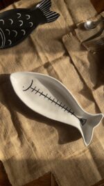 Azura Serving Platter Crafted from durable stoneware, this beautiful fish-shaped serving platter stands out with its clean white glaze and artistic hand-painted black fishbone design. It is perfect for adding a stylish sea-inspired vibe to any meal.