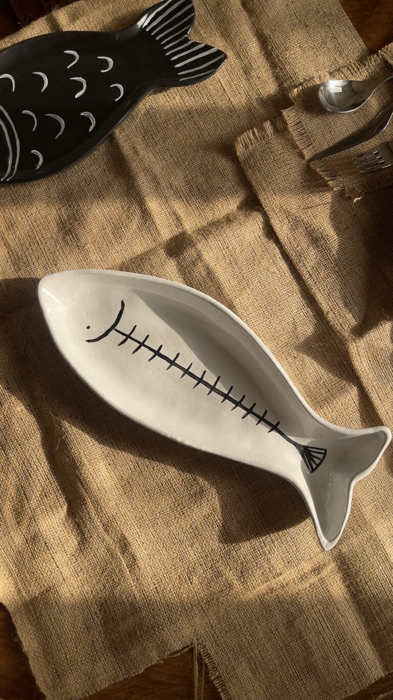 Azura Serving Platter Crafted from durable stoneware, this beautiful fish-shaped serving platter stands out with its clean white glaze and artistic hand-painted black fishbone design. It is perfect for adding a stylish sea-inspired vibe to any meal.