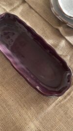 Homura Artisan Platter Captivating with its rich burgundy glaze and gently scalloped rim, this expansive stoneware platter brings a touch of dramatic warmth to your table. Its low, sleek profile makes it an exquisite backdrop for artistic food presentation or a striking accent piece for grand hosting.