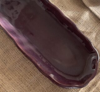 Homura Artisan Platter Captivating with its rich burgundy glaze and gently scalloped rim, this expansive stoneware platter brings a touch of dramatic warmth to your table. Its low, sleek profile makes it an exquisite backdrop for artistic food presentation or a striking accent piece for grand hosting.