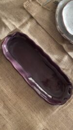 Homura Artisan Platter Captivating with its rich burgundy glaze and gently scalloped rim, this expansive stoneware platter brings a touch of dramatic warmth to your table. Its low, sleek profile makes it an exquisite backdrop for artistic food presentation or a striking accent piece for grand hosting.