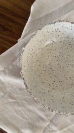 An extra-large stoneware serve bowl with a beautiful cream color and natural dark speckles. It features unique, rough edges for a natural look. With its huge size, it is perfect for serving big family salads, fruits, or hosting guests.