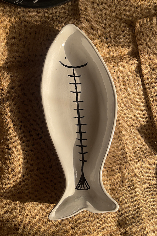 Azura Serving Platter Crafted from durable stoneware, this beautiful fish-shaped serving platter stands out with its clean white glaze and artistic hand-painted black fishbone design. It is perfect for adding a stylish sea-inspired vibe to any meal.