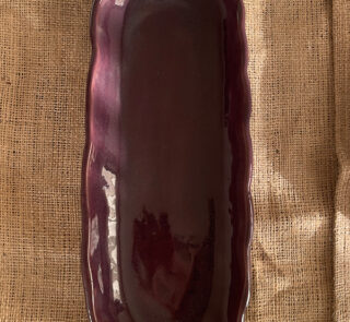 Homura Artisan Platter Captivating with its rich burgundy glaze and gently scalloped rim, this expansive stoneware platter brings a touch of dramatic warmth to your table. Its low, sleek profile makes it an exquisite backdrop for artistic food presentation or a striking accent piece for grand hosting.